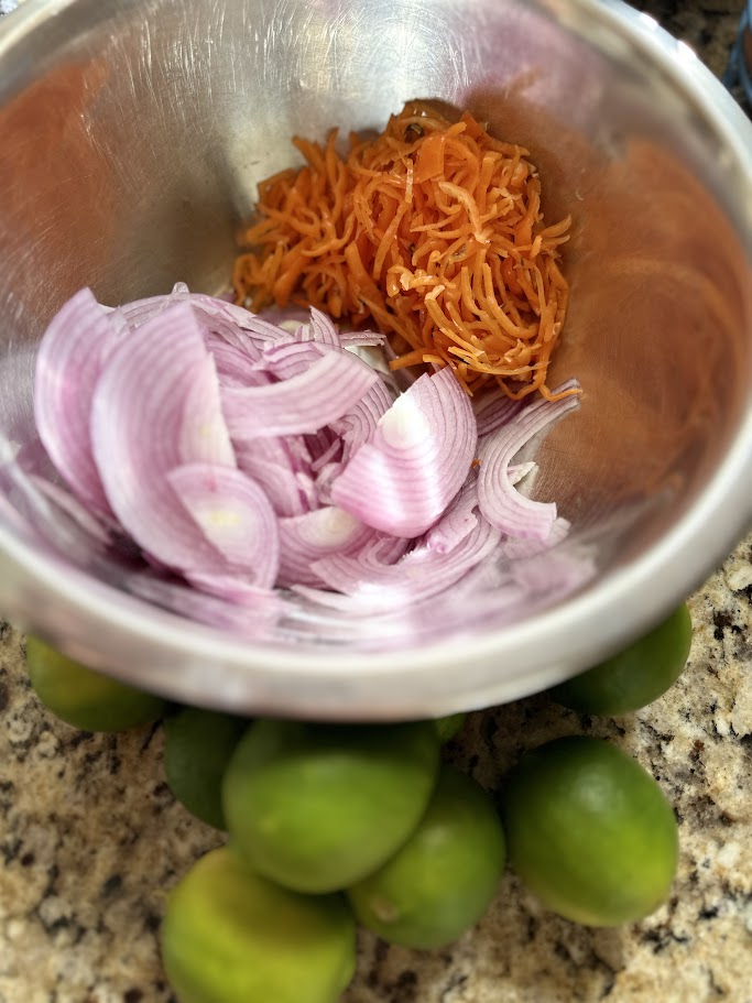 thinly sliced habanero peppers and red onions in a bowl with limes on the side.